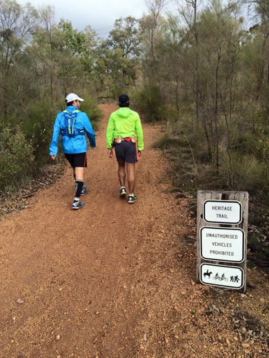 Two walkers on the gravel Railway Reserves Heritage Trail beside a trail sign