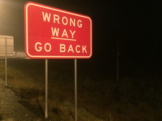 A red Wrong Way Go Back sign beside the Hume Highway in the dark.
