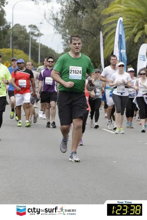 Gary running the 2013 Perth City to Surf 12 kilometre event in a green shirt with his finish time shown on the image